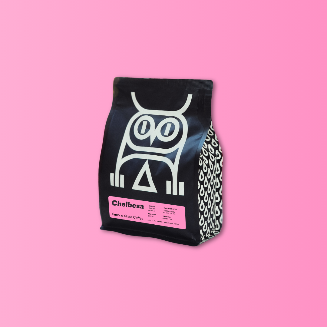 whole bean specialty coffee bag featuring white owl on black bag and text that reads Chelbesa Second State coffee. Background is gradient light to bright pink.