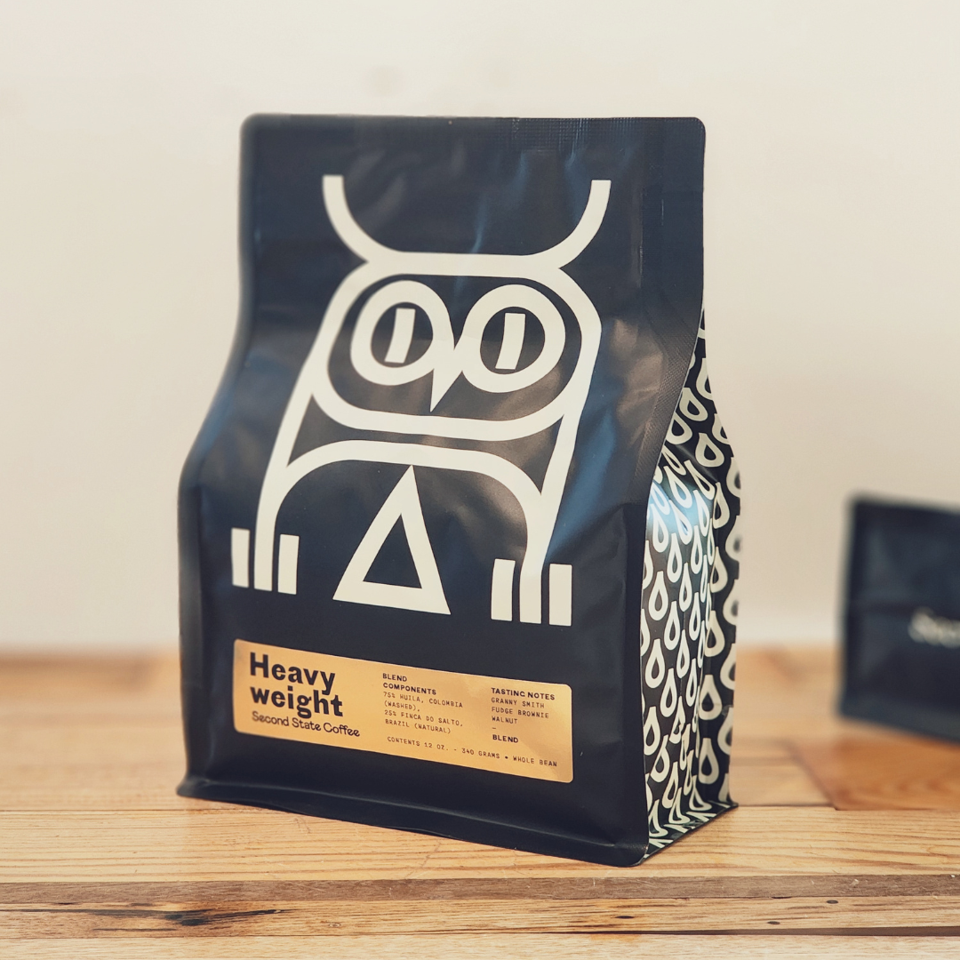 Black specialty whole bean coffee bag from Second State Coffee marked with white owl design and 'Heavy Weight' label. Sitting on a wooden counter.