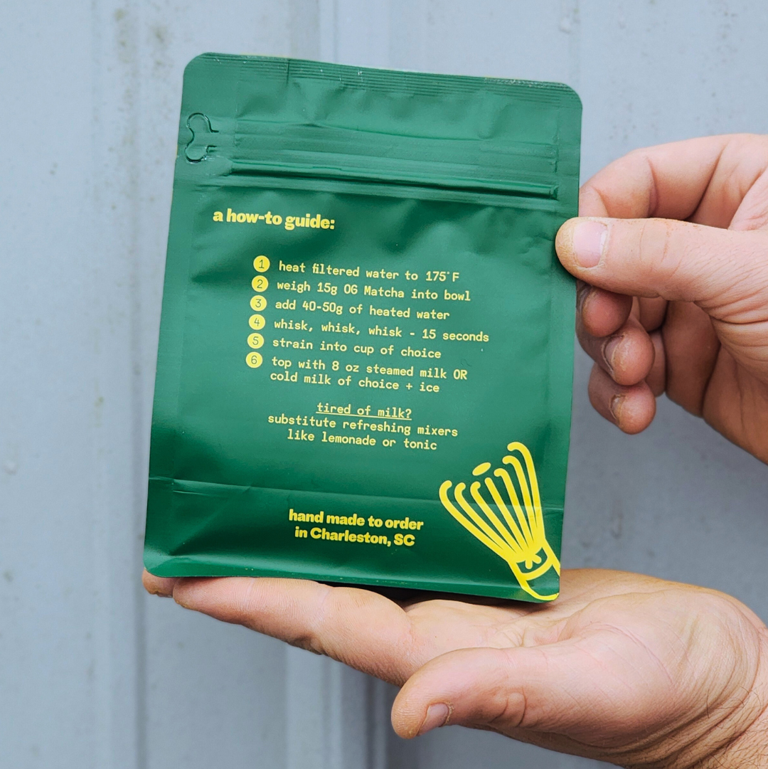 Green package with yellow text held by a hand against a gray background. og ginger sweet matcha instructions