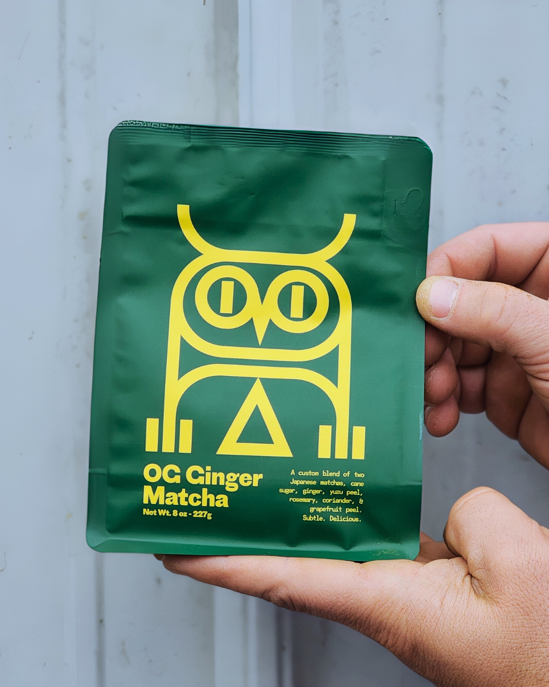 Ginger sweet matcha retail. green package with yellow owl design and text held by a hand against a light gray background.