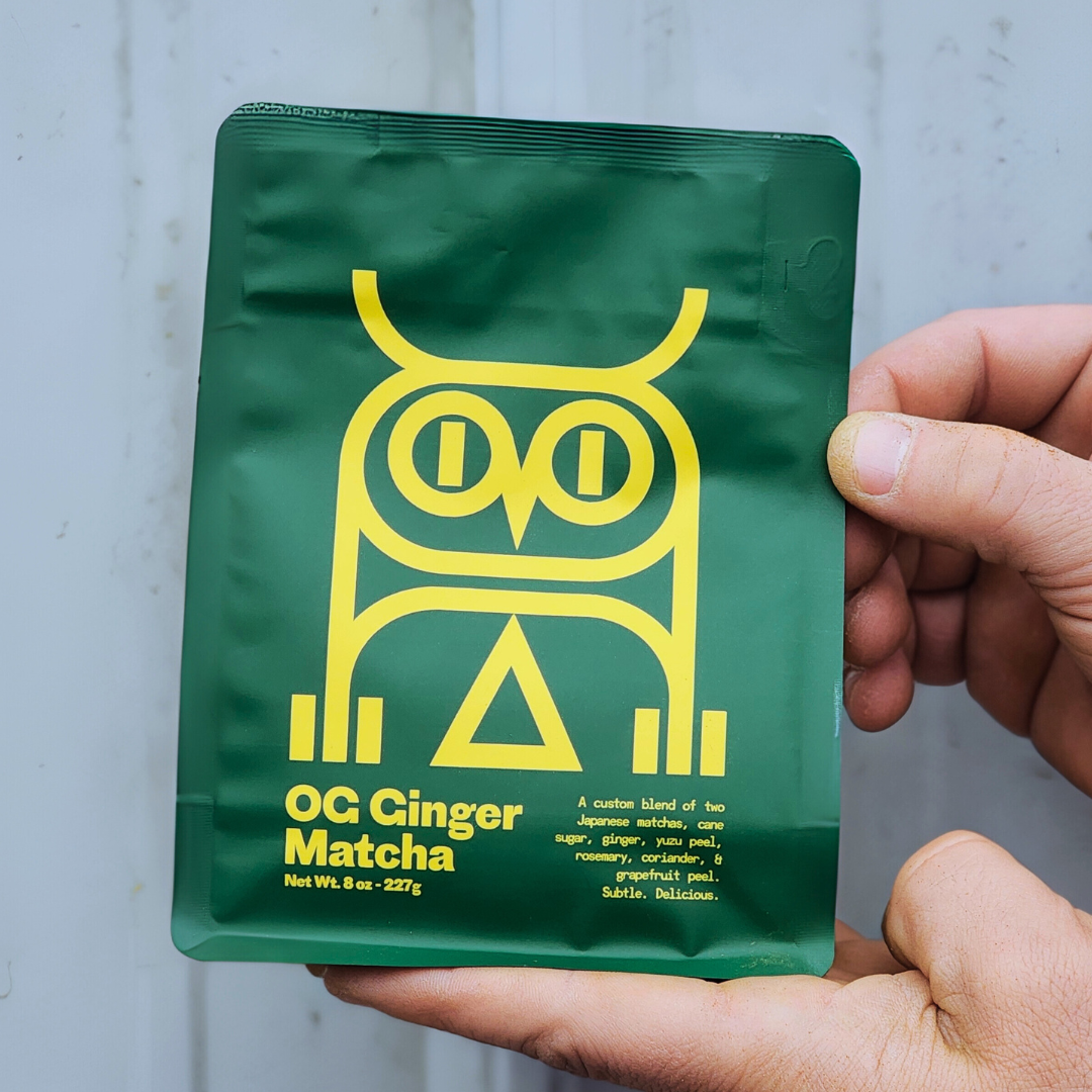 Ginger sweet matcha retail. green package with yellow owl design and text held by a hand against a light gray background.