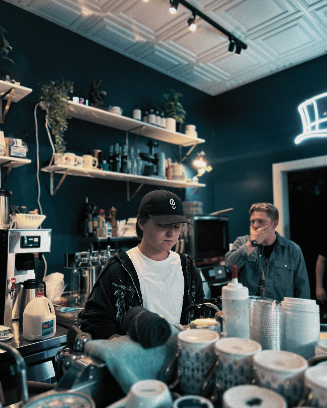 Barista working behind a counter in a coffee shop wearing black drip logo Coffee hat from second state