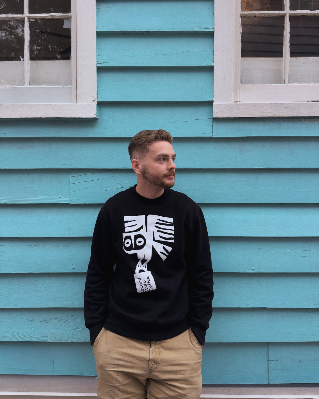 barista outside of coffee shop wearing black crew neck sweater featuring second state coffee mug and logo owl design