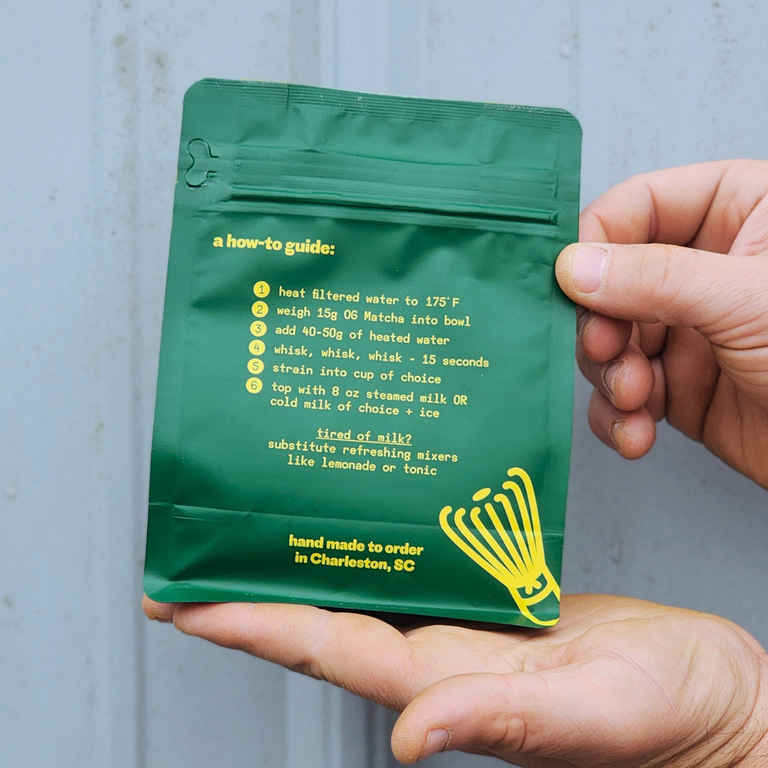 Green package with yellow text held by a hand against a gray background. og ginger sweet matcha instructions