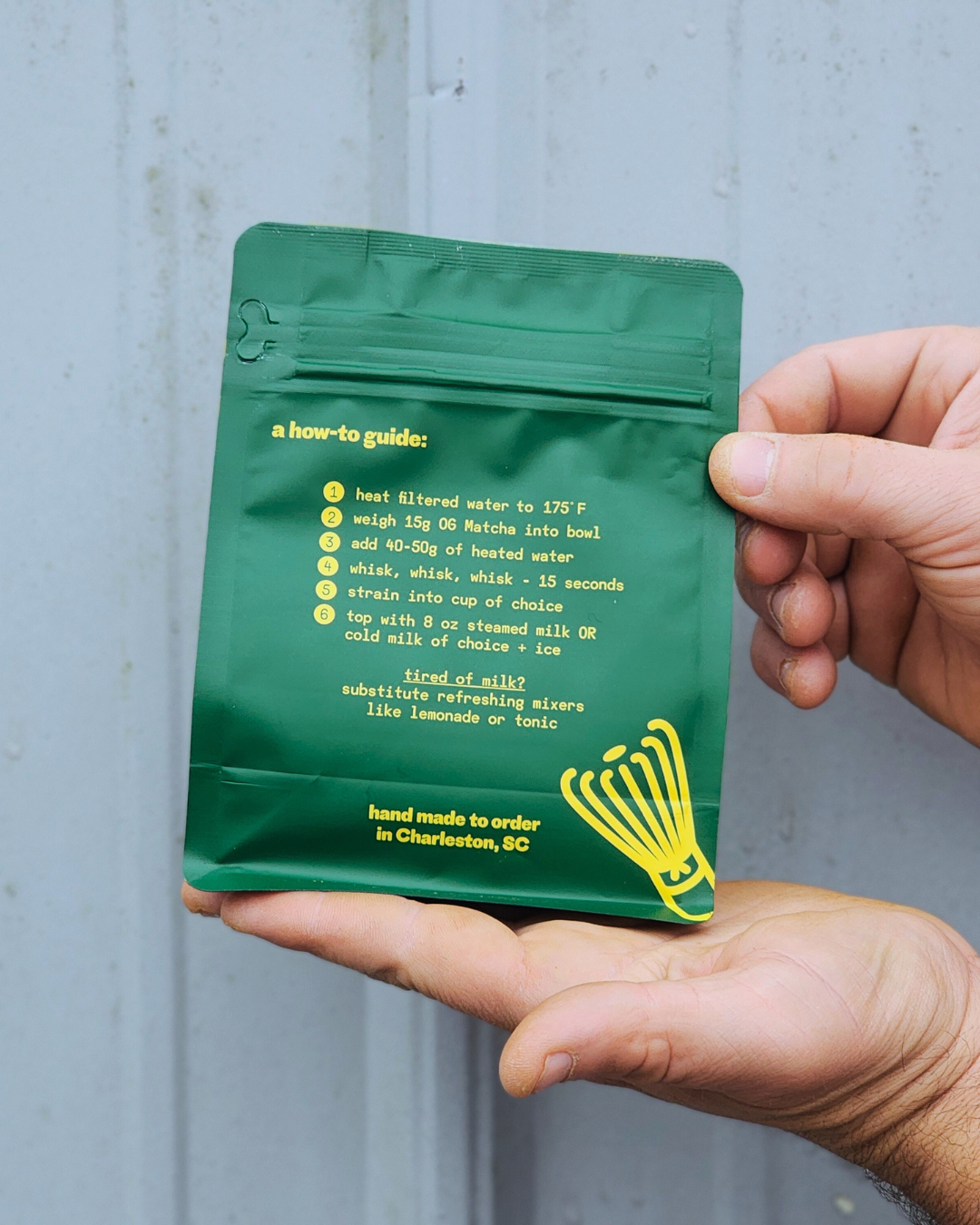Green package with yellow text held by a hand against a gray background. og ginger sweet matcha instructions
