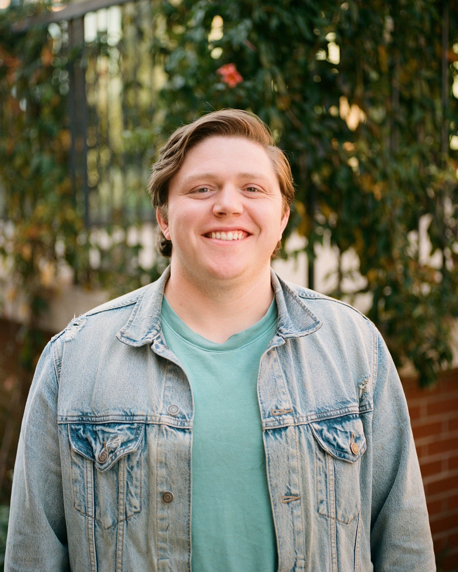 person wearing a denim jacket over a green shirt with a blurred natural background